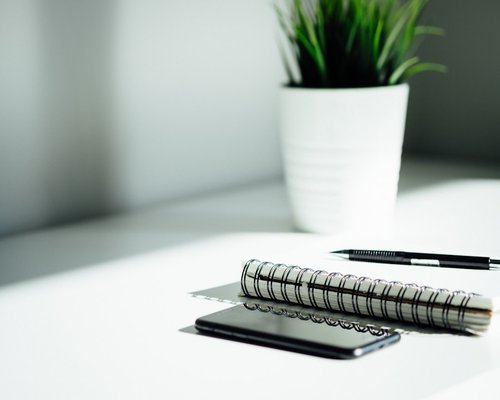 A modern and clean office desk with a plant and notepad